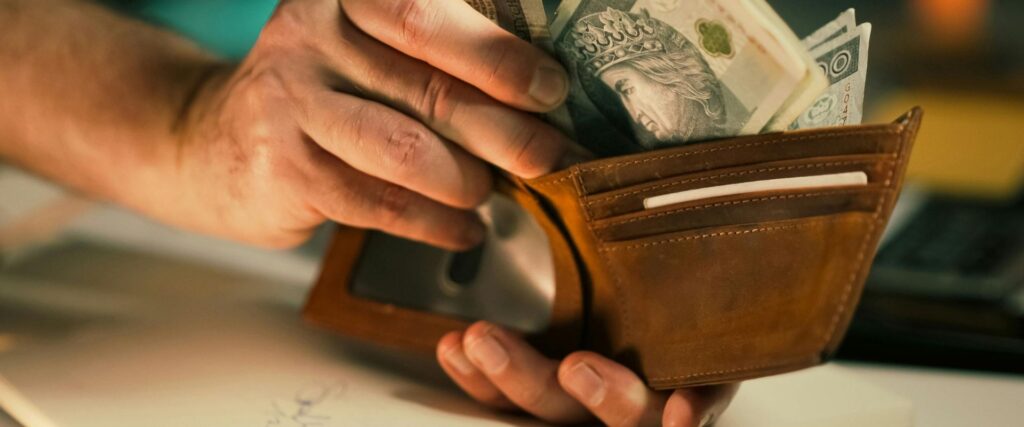 Zdjęcie przedstawia banknoty wyjmowane z portfela nawiązujące do odszkodowania gminy za niedostarczenie lokalu socjalnego